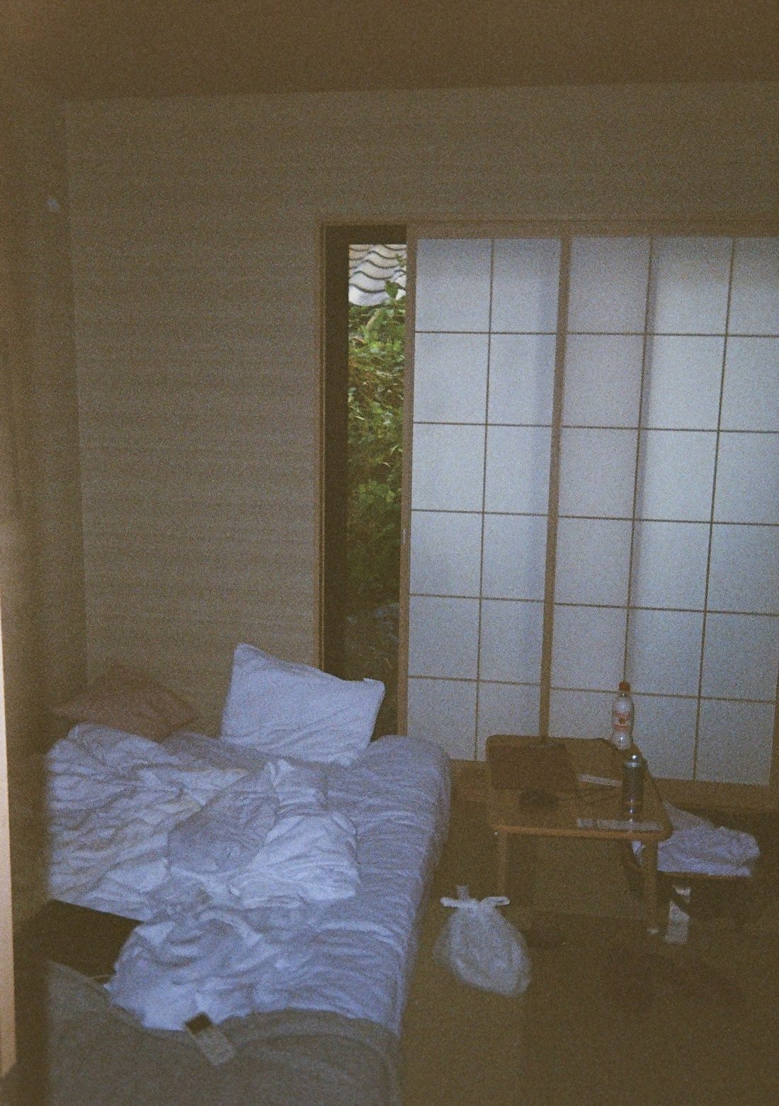 A quiet tatami room at dusk — a futon on the floor, a low table and a shoji screen with a sliver of garden showing through