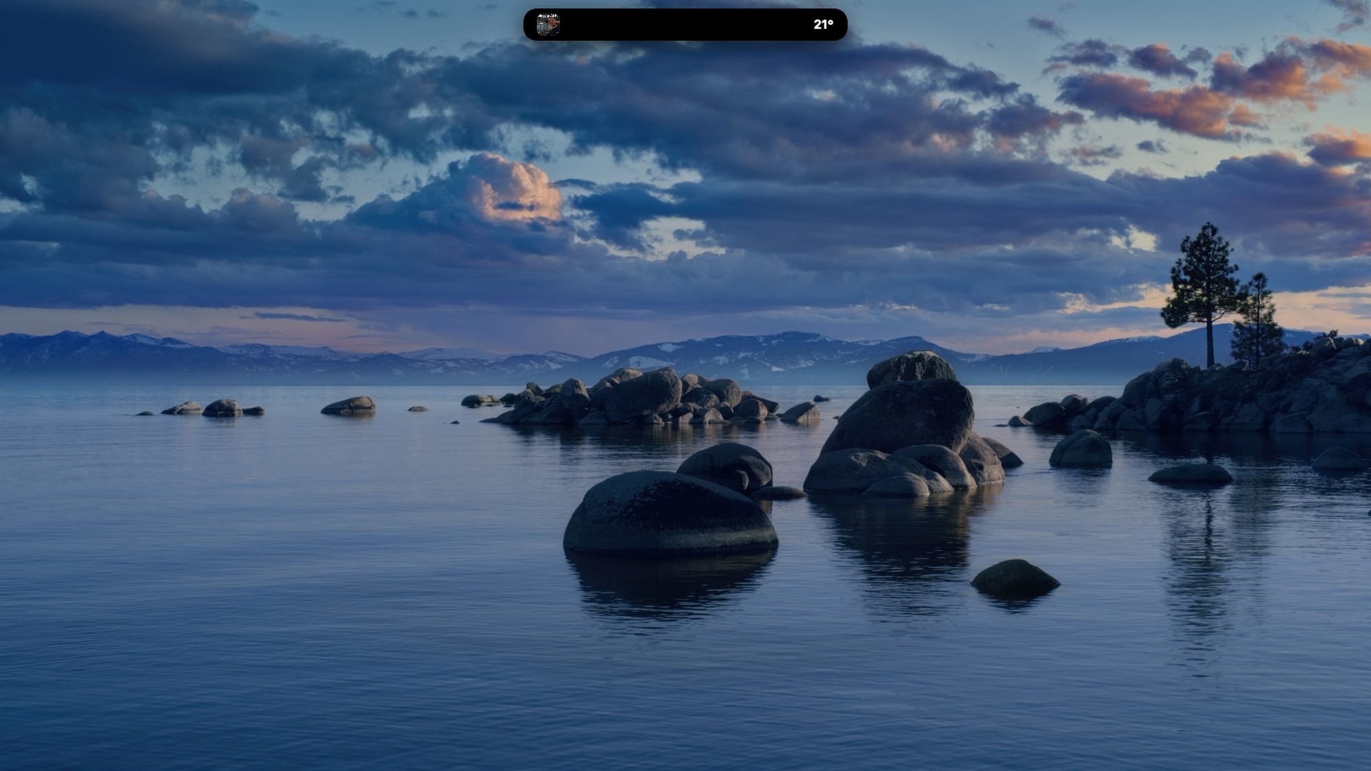 All in a notch in Dynamic Island mode — the closed notch as a black pill at the top of the desktop showing album art and the current temperature, 21 degrees